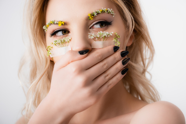 naked beautiful blonde woman with wildflowers under eyes covering mouth isolated on white - Photo, Image