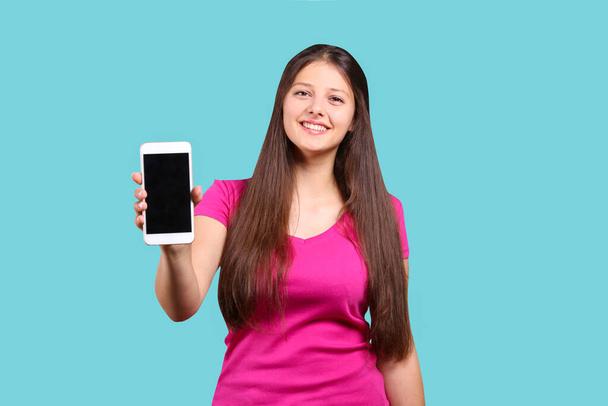 Young beautiful curvaceous woman posing with new phone over isolated background with a lot of copy space for text. Portrait of attractive female with long brunette hair wearing loose pink t-shirt. - Foto, imagen