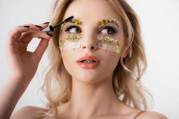 beautiful blonde woman styling wildflowers on eyebrows with brow gel isolated on white - Fotó, kép