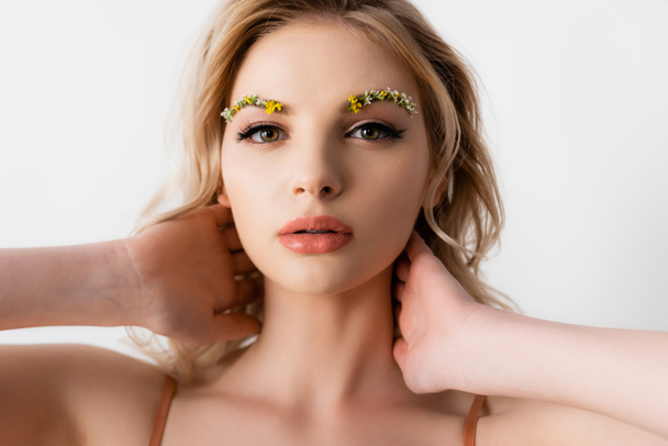 belle femme blonde avec des fleurs sauvages sur les sourcils touchant le cou isolé sur blanc - Photo, image