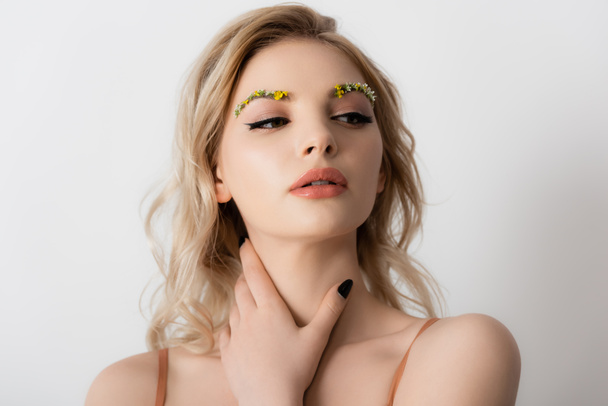 beautiful blonde woman with wildflowers on eyebrows touching neck isolated on white - Foto, Imagen