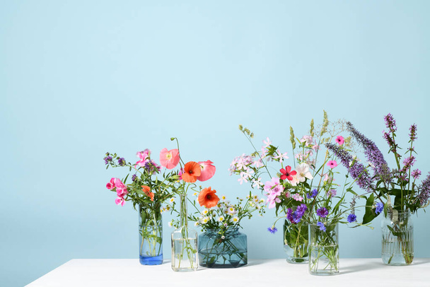 Glass vases with beautiful wildflowers on blue background - Fotó, kép