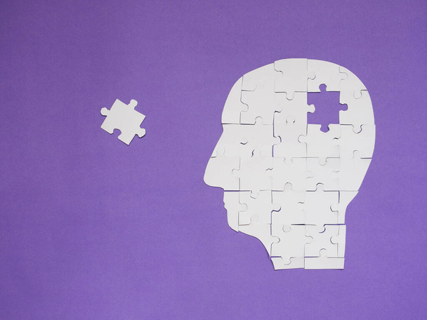 Head brain white puzzle with missing pieces from jigsaw puzzle on purple background. Creative idea for memory loss, dementia, Alzheimer's disease and mental health concept. Copy space. - Photo, Image