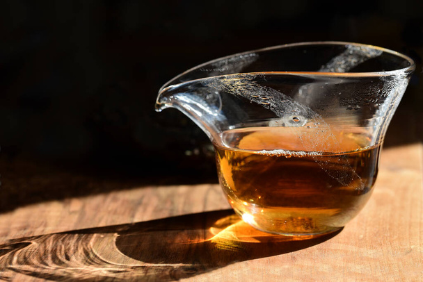 Lähikuva kiinalainen lasi teekannu musta tuoretta teetä seisoo pöydällä tummaa taustaa vasten auringonvalo paistaa sen läpi - Valokuva, kuva