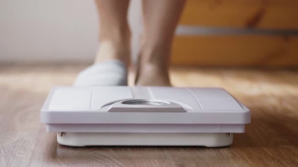 Primer plano de la joven mujer asiática comprobando el peso corporal en la báscula de pesaje en la sala de estar en casa. - Metraje, vídeo