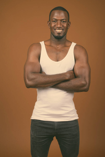 Studio colpo di bel muscoloso uomo africano indossa canotta contro sfondo marrone - Foto, immagini