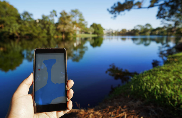 Homem usando aplicativo de mapa móvel ao lado do lago
 - Foto, Imagem
