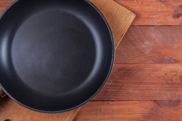 Black frying pan on a wooden table and many different vegetables - Photo, Image