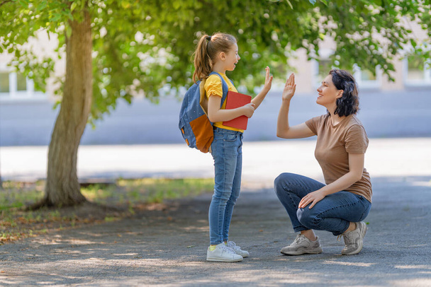 Parent and pupil of secondary school going hand in hand. Woman and girl with backpack behind the back. Beginning of lessons. First day of fall. - Foto, Imagen