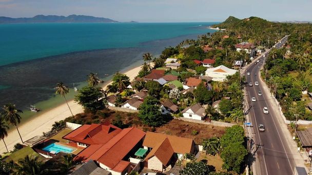 Deniz kıyısındaki evler ve yollar. Tayland 'ın güneşli bir gününde Ko Samui Adası' ndaki ana yol ve kıyı kulübelerinin insansız hava aracı görüntüsü. Bang Po egzotik tropik plajı - Fotoğraf, Görsel