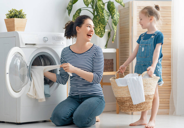 Güzel genç kadın ve kız çocuk küçük yardımcı evde çamaşır yıkarken eğleniyor ve gülümsüyor.. - Fotoğraf, Görsel