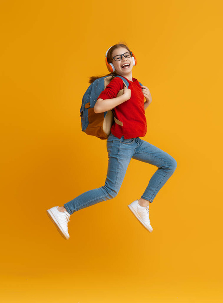 Back to school and happy time! Cute industrious child is jogging on color paper wall background. Kid with backpack. Girl ready to study. - Fotó, kép