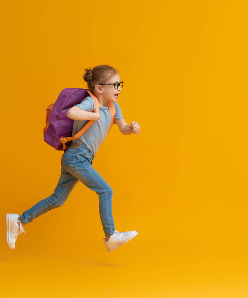 Back to school and happy time! Cute industrious child on color paper wall background. Kid with backpack. Girl ready to study. - Zdjęcie, obraz