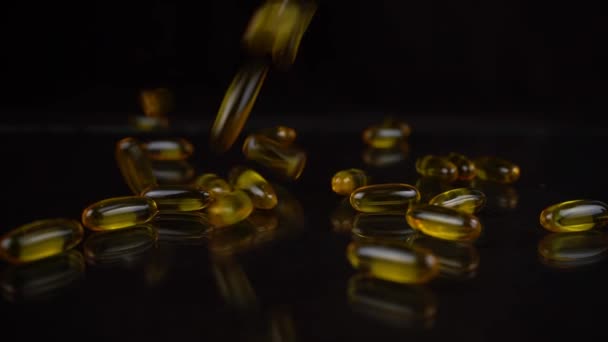 Zeitlupenaufnahme fallender Omega-3-Fischöl-Kapseln auf schwarzem Spiegelhintergrund. Goldfarbene Vitamine in Gelhülle - Filmmaterial, Video