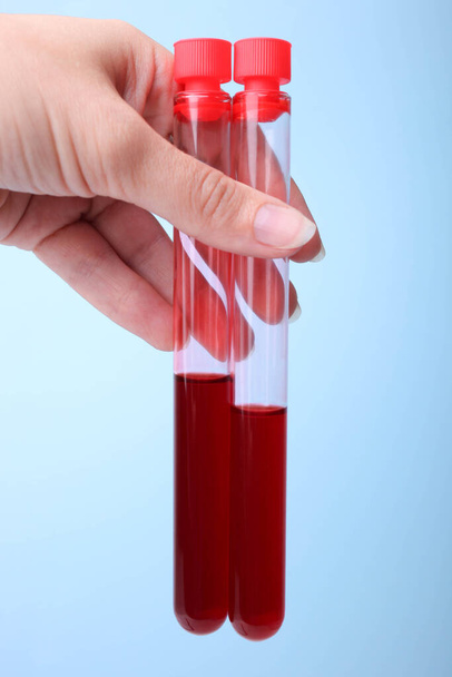 Testbuisjes met bloed in een vrouwelijke hand op een blauwe achtergrond. Concept analyseert. - Foto, afbeelding