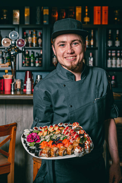 Portret van chef-kok in café met bord met sushi - Foto, afbeelding
