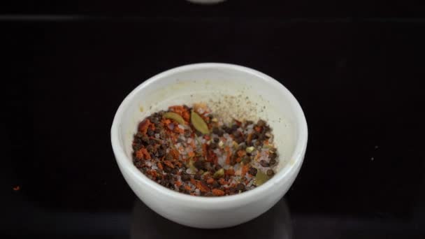 Variedad de especias y sal machacando en un tazón blanco especial con el chorrito sobre fondo negro
 - Metraje, vídeo