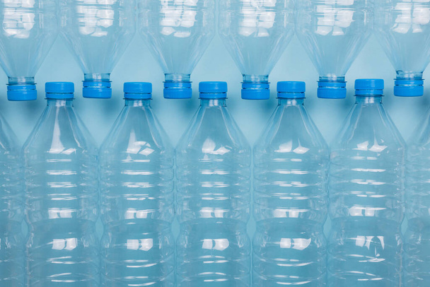 Poziomy obraz koloru z widokiem z przodu pustych przezroczystych plastikowych butelek z nakrętkami ułożonymi na niebieskim tle. Koncepcja recyklingu i ochrony środowiska. - Zdjęcie, obraz
