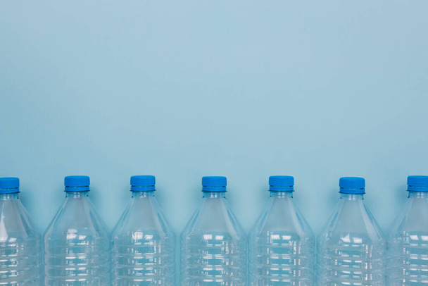 Horizontales Farbbild mit einer Frontansicht einer leeren klaren Plastikflasche mit Deckeln auf blauem Hintergrund. Recycling- und Umweltkonzept. - Foto, Bild