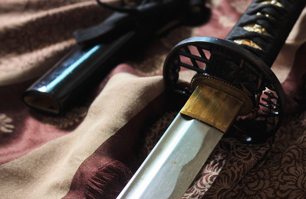 крупным планом японский меч такана на атласе с теплыми цветами падения, мягкий фокус на заднем плане. над светом - Фото, изображение