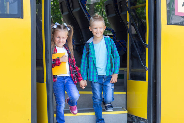 Χαρούμενα παιδιά με σακίδια κατεβείτε από το σχολικό λεωφορείο. - Φωτογραφία, εικόνα