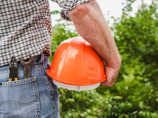 Attractive man with tools, holding a safety helmet. View from the back, close-up. Concept of work and employment - Foto, Imagem