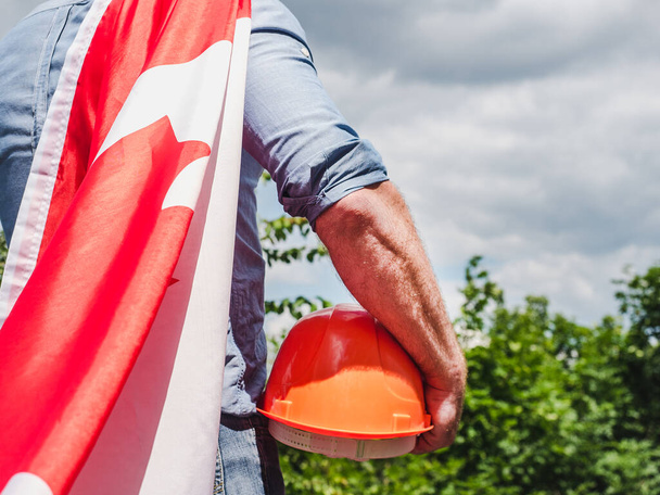 Attractive man holding a Canadian Flag on blue sky background on a clear, sunny day. View from the back, close-up. National holiday concept - Foto, Imagen