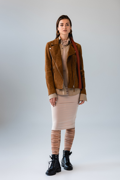 full length view of attractive girl in fashionable autumn clothes looking at camera while posing on grey - Foto, afbeelding