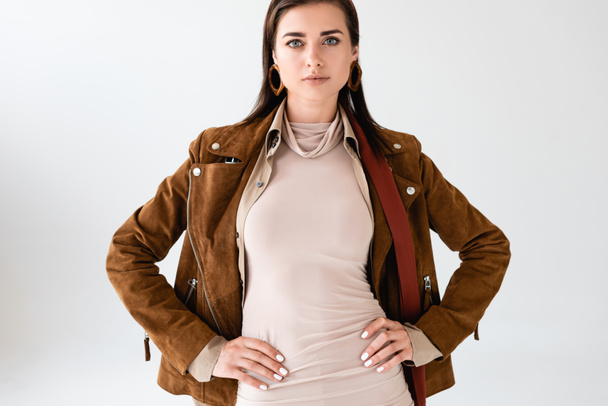 confident, trendy girl in suede jacket posing with hands on hips isolated on grey - Foto, Imagem