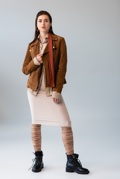 full length view of attractive girl in trendy autumn outfit touching suede jacket on grey - Fotoğraf, Görsel