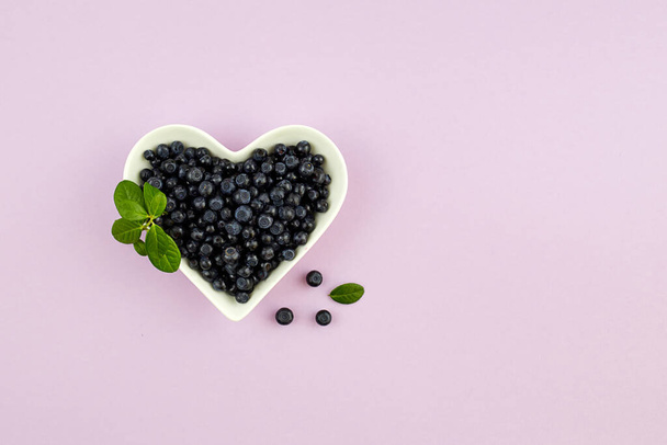 Blueberries in bowl in the shape of a heart on a lilac background - Foto, Imagen