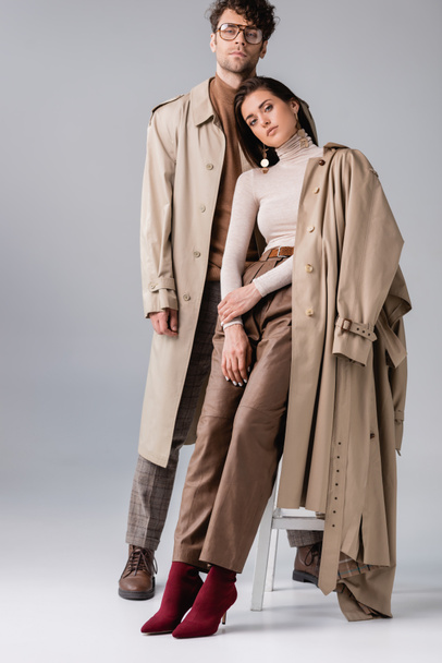 full length view of young couple in trendy autumn clothes looking at camera on grey - Photo, Image