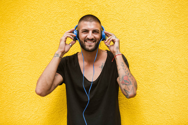 Porträt eines Tätowierers, der freudig Musik auf Headsets hört. Gelber Hintergrund. - Foto, Bild