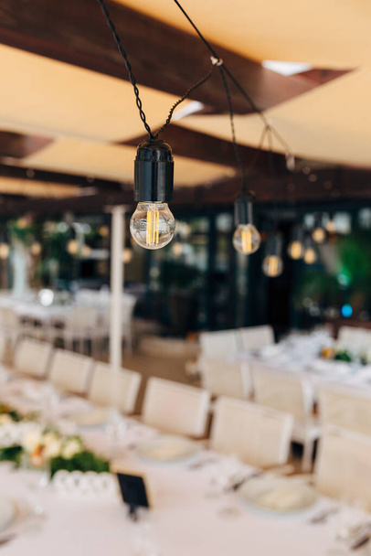 Γιρλάντες από λαμπτήρες LED πάνω από ένα τραπέζι δεξιώσεων για ένα γαμήλιο δείπνο. - Φωτογραφία, εικόνα