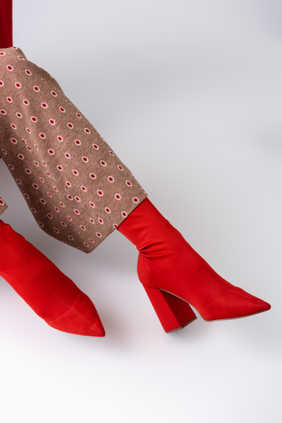 przycięty widok modnej kobiety w beżowych spodniach i czerwonych butach siedzącej na białej podłodze - Zdjęcie, obraz