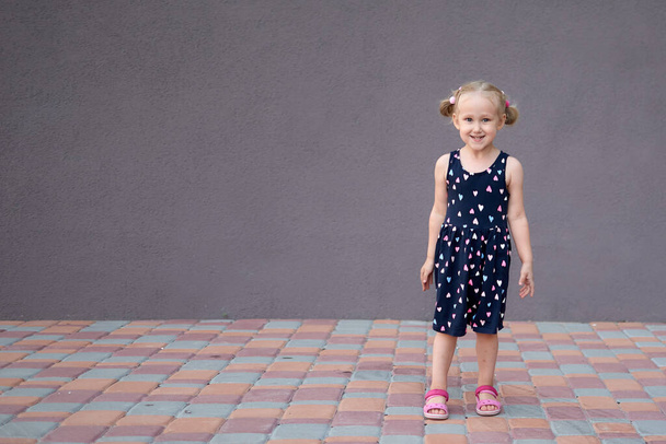 幸せな小さな金髪の女の子の肖像画をクローズアップ。3歳の白人幼児の女の子が屋外の散歩で笑っています。コピースペースと石の壁の背景 - 写真・画像