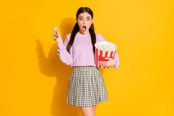 Portrait of astonished girl watch tv see unbelievable horror series impressed scream wow omg eat big pop corn box wear checkered pullover isolated over shine color background - Foto, Bild