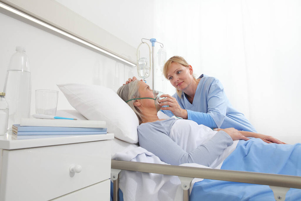 nurse puts oxygen mask on elderly woman patient lying in the hospital room bed - Фото, изображение