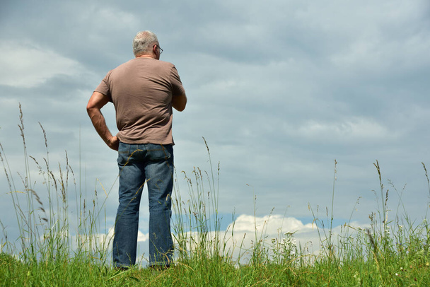 Een man staat in een weide tegen een bewolkte lucht en kijkt in de wolken - Foto, afbeelding