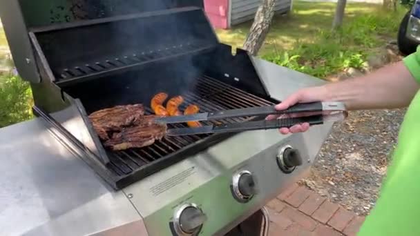 Styl życia lato odkryty człowiek gotowanie kołki i kiełbasy na gazowym grillu dziurkowanie metalowe języki - Materiał filmowy, wideo