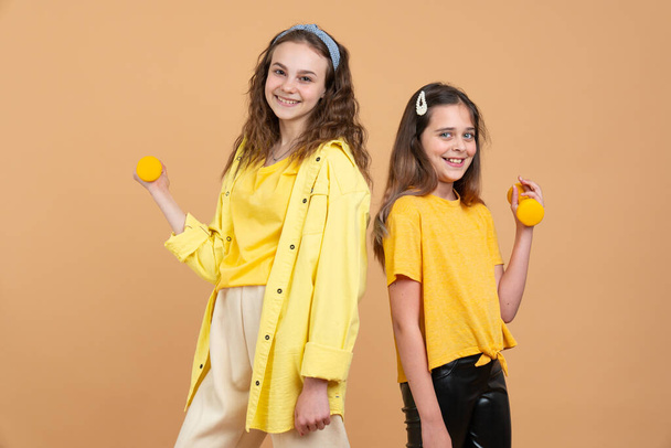 Duas crianças jovens brincalhão em camisas amarelas, irmãs ou pré-adolescentes meninas biraciais com cabelo encaracolado marrom brincando ou exercitando, levantando halteres
 - Foto, Imagem