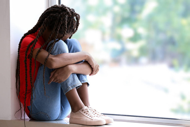 Surullinen afroamerikkalainen tyttö istuu ikkunalaudalla. Lopeta rasismi - Valokuva, kuva
