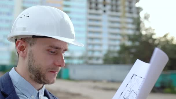 Close-up, een ingenieur in een witte helm houdt bouwtekeningen in zijn handen - Video