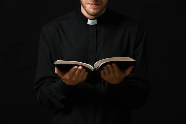 Handsome priest with Bible on dark background - Photo, Image