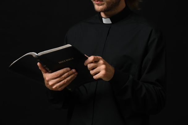 Jóképű pap Bibliával sötét háttérrel - Fotó, kép