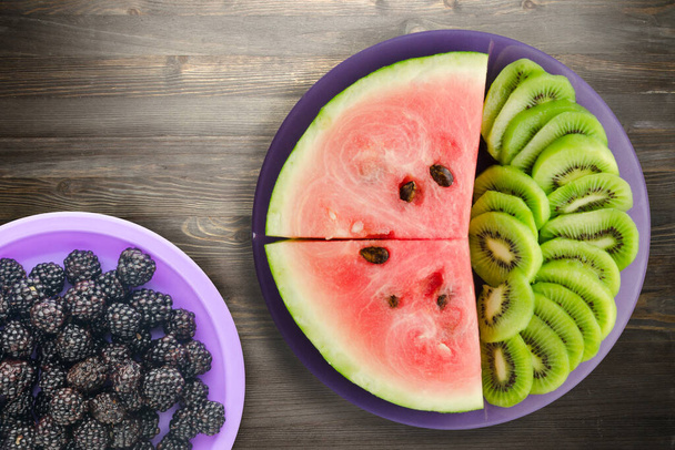 watermelon and kiwi sliced on a purple plate on a black wooden background .fruits on a plate  - Фото, зображення