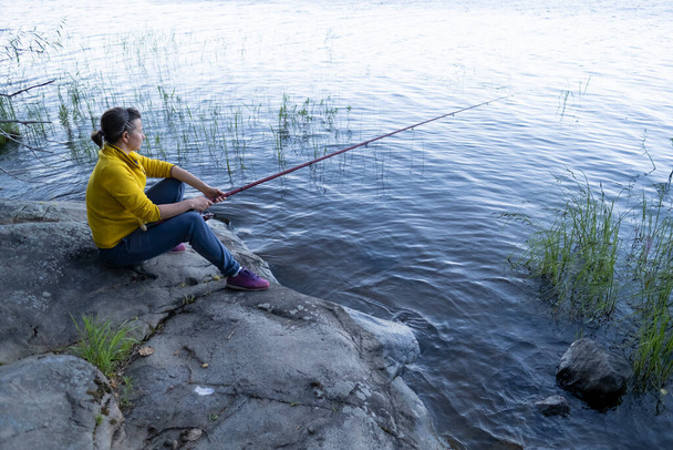 Fishing woman sitting on stone near lake - Fotoğraf, Görsel
