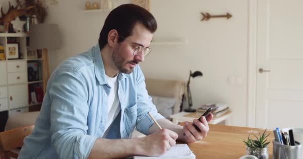 Uomo tenere smartphone prende informazioni da internet scrittura su notebook - Filmati, video
