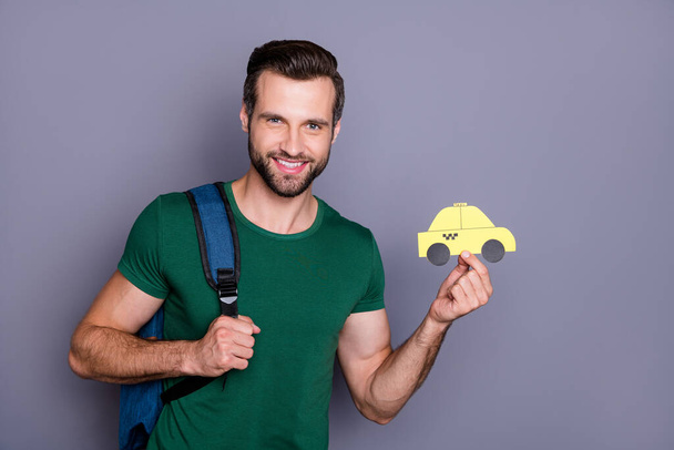 Portrait of positive cheerful guy hold paper card taxi enjoy travel trip tour transport service wear bag green t-shirt isolated over gray color background - Zdjęcie, obraz