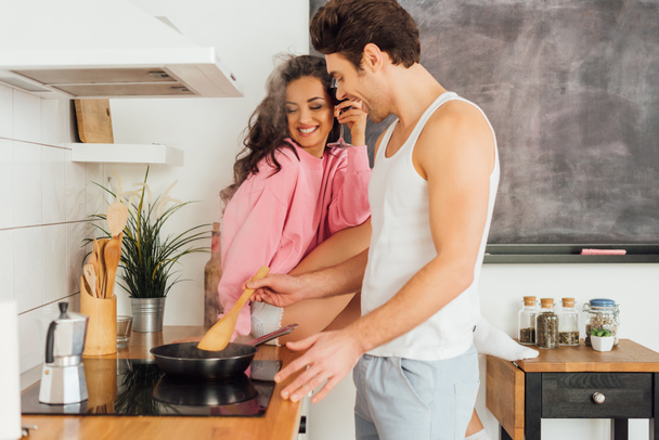 Enfoque selectivo de hombre alegre cocina cerca de mujer hermosa sosteniendo vaso de vino en encimera de la cocina
  - Foto, Imagen